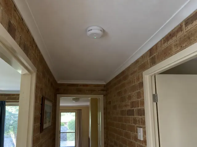 Ceiling-mounted smoke alarm in a brick hallway with white trim in Croudace Bay